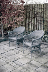 Fototapeta na wymiar Woven armchairs outside in a rustic garden with autumn plants for relaxing after gardening. Yard landscape with two wooden chairs in nature in a backyard patio to enjoy peace and quite of winter