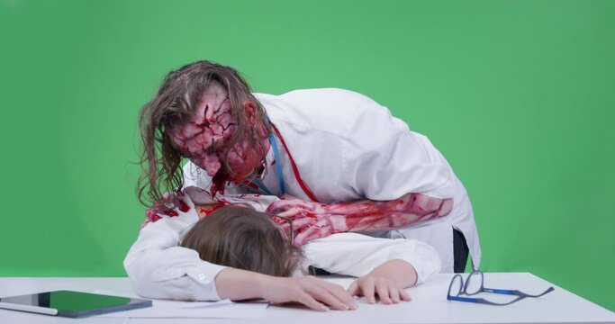 Furious zombie in doctor coat attacks and eats dead young woman. Hungry spooky man with mustache and covered with blood eats flesh of nurse corpse on green chrome key.
