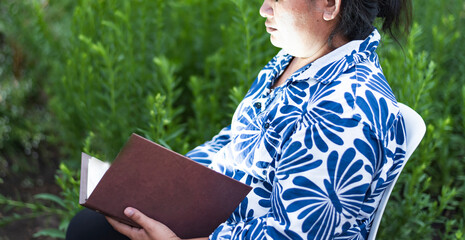 A young Asian woman with black hair sits on a reading chair against a flower garden background.