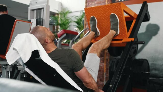Muscular man using weights machine for legs at the gym. Hard training. High quality 4k footage