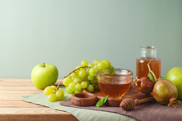 Still life with honey jar, green apples, grapes and pomegranate on wooden table. Jewish holiday...