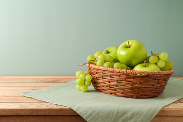 Green apples and grapes in basket on wooden table with tablecloth. Kitchen background