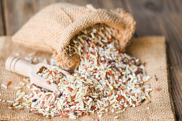 brown rice in the sack with wooden background , raw various rice color mixed thai rice for cooking food , Loonzain rice brown black red white purple health food.