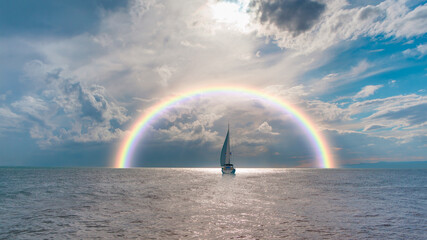 Yacht sailing in open sea at stormy day - Anchored sailing yacht on calm sea with tropical storm and double sided rainbow in the background - obrazy, fototapety, plakaty