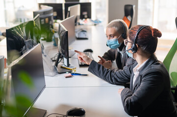 Two women in medical masks and headsets are working in the office