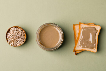 Sunflower paste in a small bowl, a jar and a piece of bread. A modern alternative to nut paste