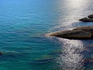 Beautiful seascape of turquoise blue sea with silver glares on the waves at evening dusk. Scenic coastal rocks in the sea shore. 