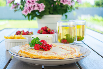 Pancakes with caramelized apples, raspberries, strawberries and red currants. Brunch with green tea and crepes.