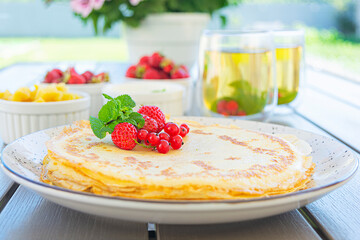 Pancakes with caramelized apples, raspberries, strawberries and red currants. Brunch with green tea and crepes.