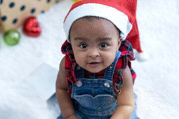 African American baby girl wearing Santa hat sitting on fur in room, Christmas time, Holiday season, looking at camera