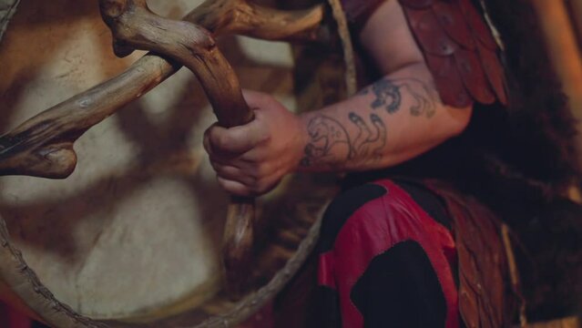 Man supports shamanic traditions and plays ritual drum at performance on stage closeup. Musician plays tribal instruments. Folk band show