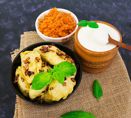 Delicious dumplings with cabbage and sour cream on dark background