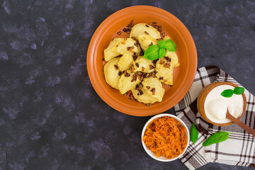 Delicious dumplings with cabbage and sour cream on dark background. Top view