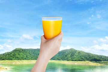 woman holding a glass of orange juice with mountain background beautiful sky Fresh orange juice concept contains vitamin C for health benefits.