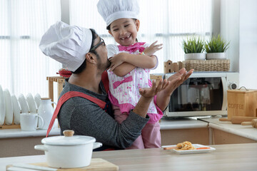 Father and daughter playing in the kitchen and having fun, both wearing chef hat and apron