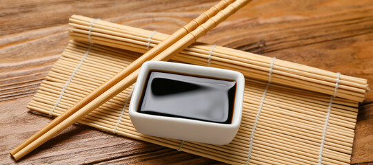 Bowl of soy sauce, bamboo mat and chopsticks on wooden background