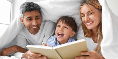 Happy parents reading book to their little son in bed