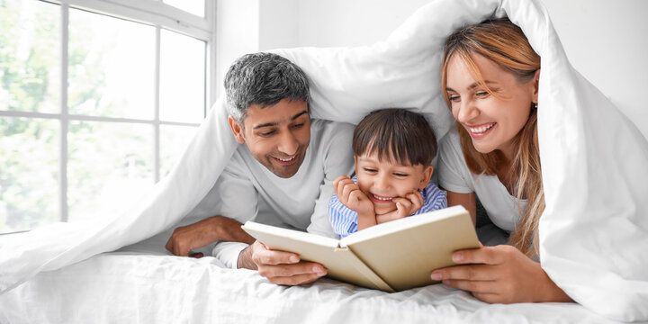 Happy parents reading book to their little son in bed