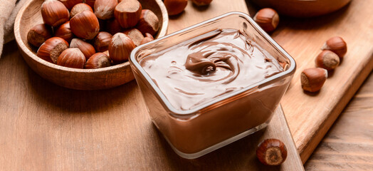 Bowl with tasty chocolate paste and hazelnuts on wooden background