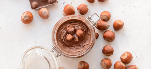 Jar with tasty chocolate paste and hazelnuts on light background, top view