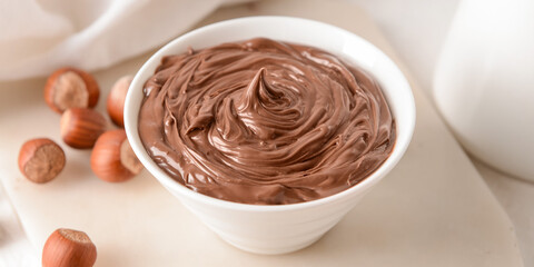 Bowl with tasty chocolate paste and hazelnuts on light table, closeup
