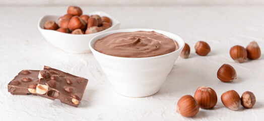Bowl with tasty chocolate paste and hazelnuts on light table