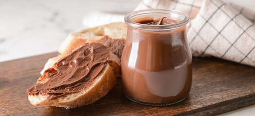 Jar with tasty chocolate paste and bread on table