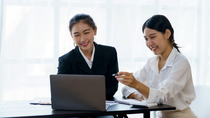 Two professional Asian business women discuss work using a laptop computer to work in the office.