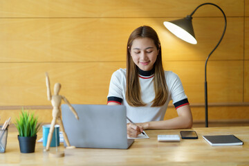 Beautiful young Asian woman student studying online with laptop computer at home.