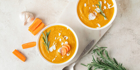 Bowls of tasty carrot cream soup on light background, top view