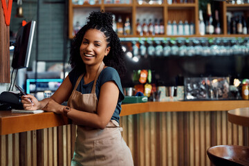 Happy African American waitress at bar counter in cafeteria looking at camera. - obrazy, fototapety, plakaty