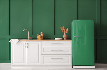 Kitchen counter with sink and retro fridge near green wall