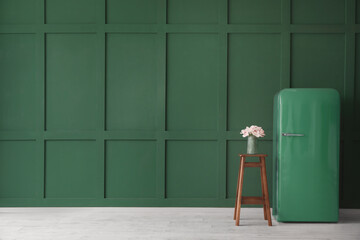 Stylish retro fridge and stool with flowers in vase near green wall