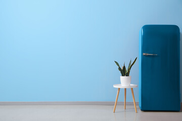 Stylish retro fridge and table with houseplant near blue wall
