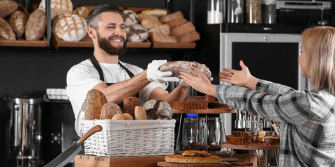 Male baker giving fresh bread to client in shop - obrazy, fototapety, plakaty