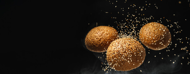 Flying burger buns with sesame seeds on black background with space for text