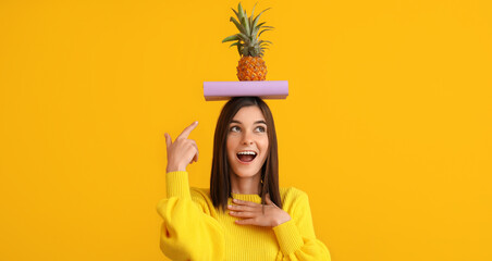 Beautiful happy young woman with book and pineapple on yellow background