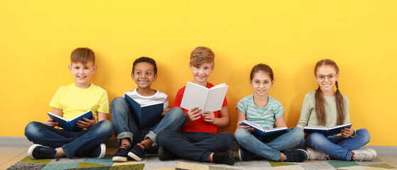 Cute little children reading books on yellow background