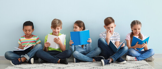 Cute little children reading books on light blue background