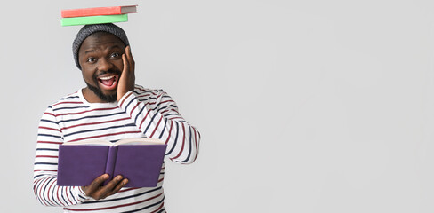 Surprised African-American man reading books on light background with space for text