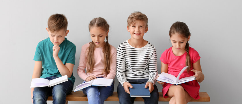 Cute little children reading books on grey background
