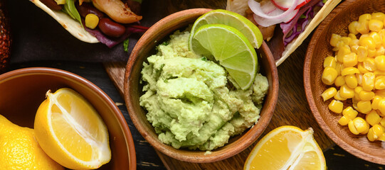 Bowls with tasty guacamole, corn and lemons on table, top view