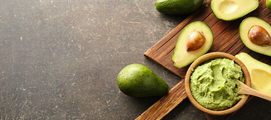 Wooden board with bowl of delicious guacamole and ripe avocados on grey background with space for text