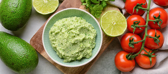 Bowl with tasty guacamole, tomatoes, avocados and lime on light background
