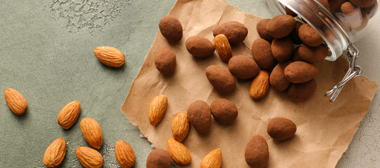 Overturned jar with tasty chocolate almonds on grey background
