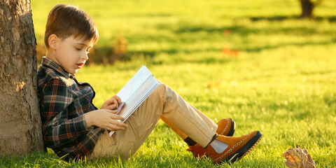 Cute little boy reading book in park