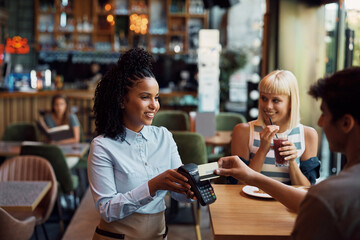 Happy black waitress accepting payment by credit card in cafe.