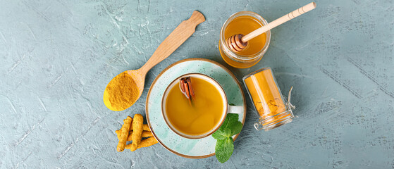 Cup of healthy turmeric drink, powder and jar of honey on grey background