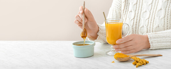 Woman with cup of healthy turmeric drink and honey in bowl on table