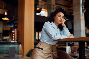 Pensive African American waitress looking away in cafe.